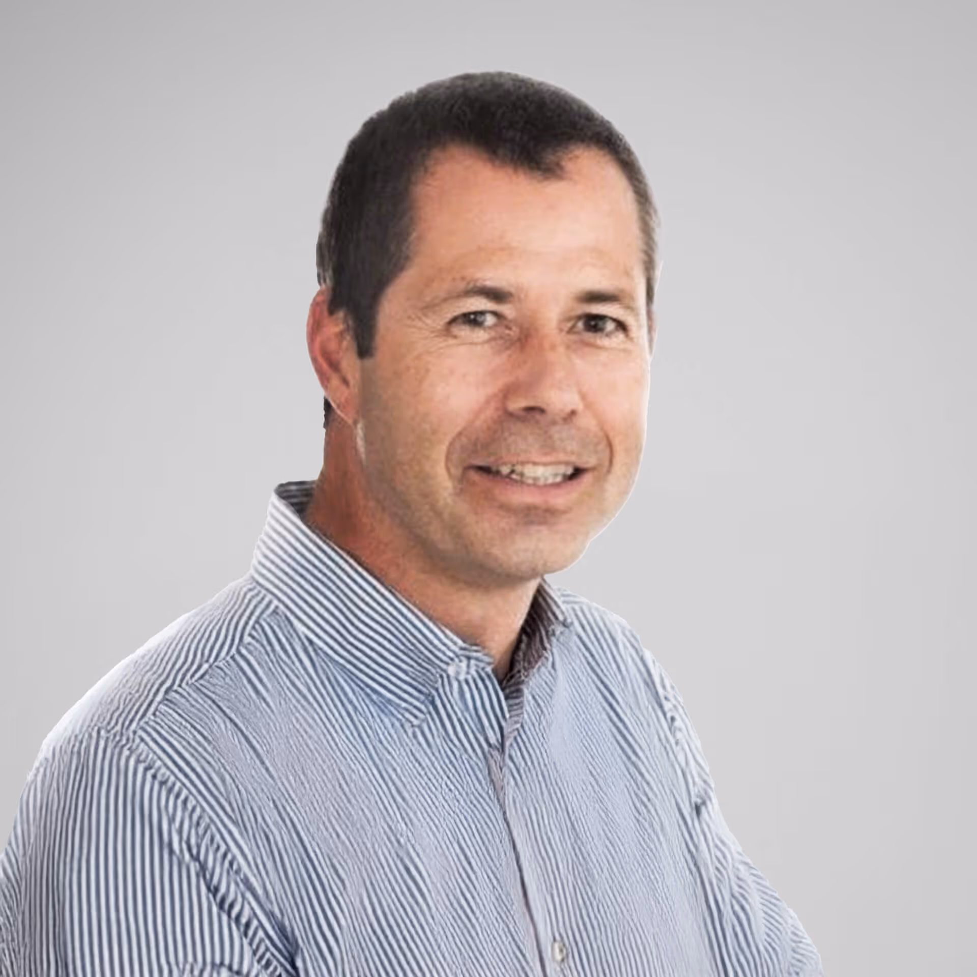 Smiling man with short dark hair wearing a blue and white striped button-up shirt against a light gray background.