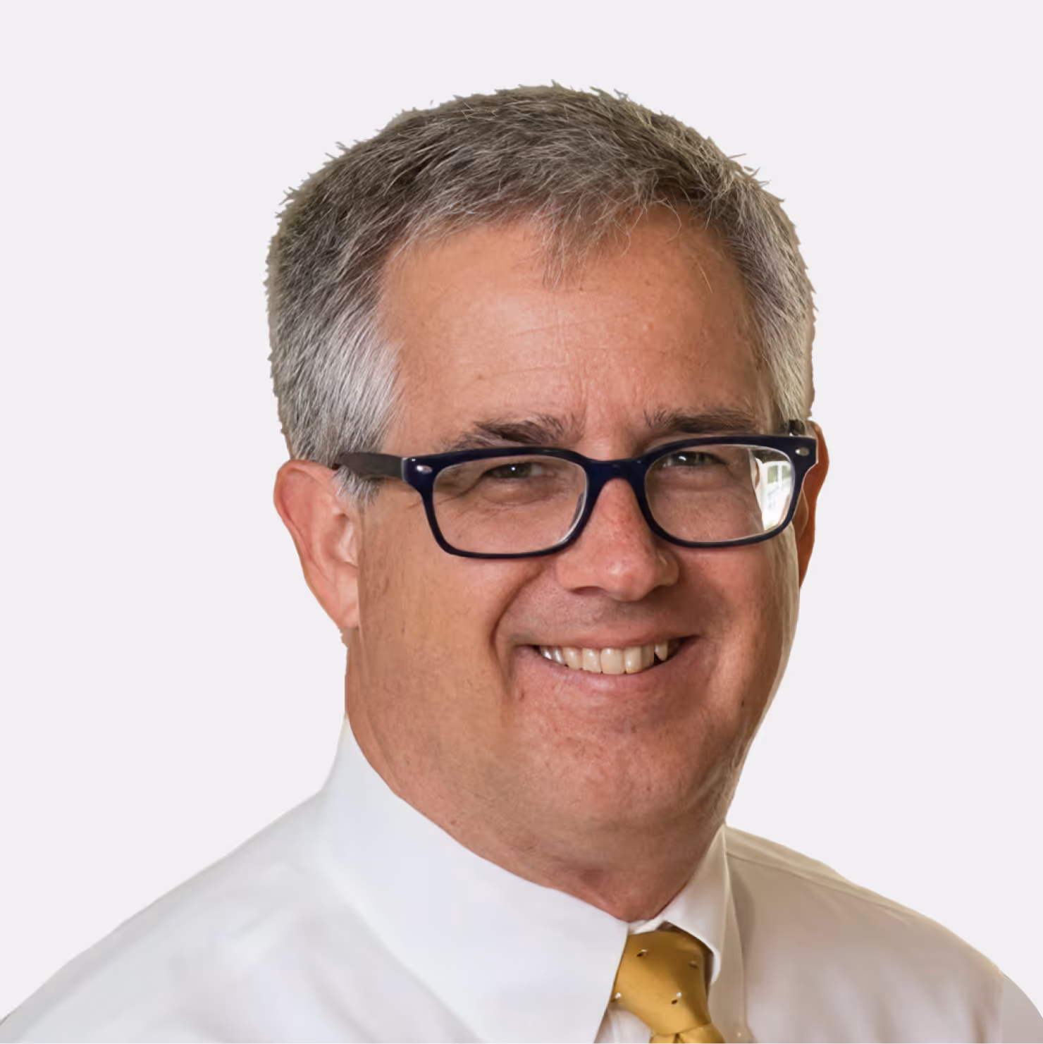 Smiling middle-aged man with gray hair and glasses wearing a white shirt and yellow tie.