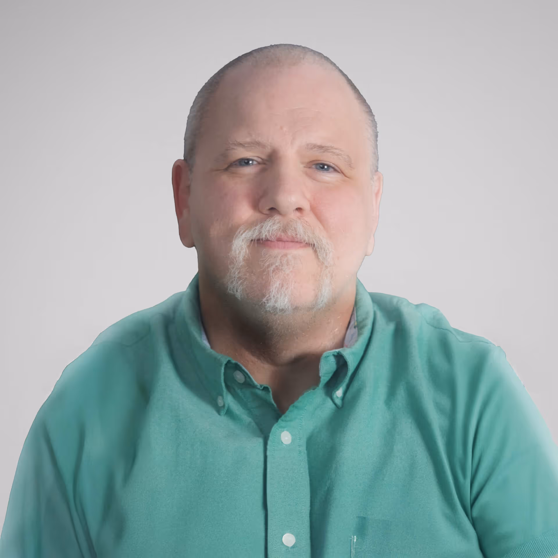 Middle-aged man with a mustache and goatee wearing a green button-up shirt, looking straight at the camera with a neutral expression.