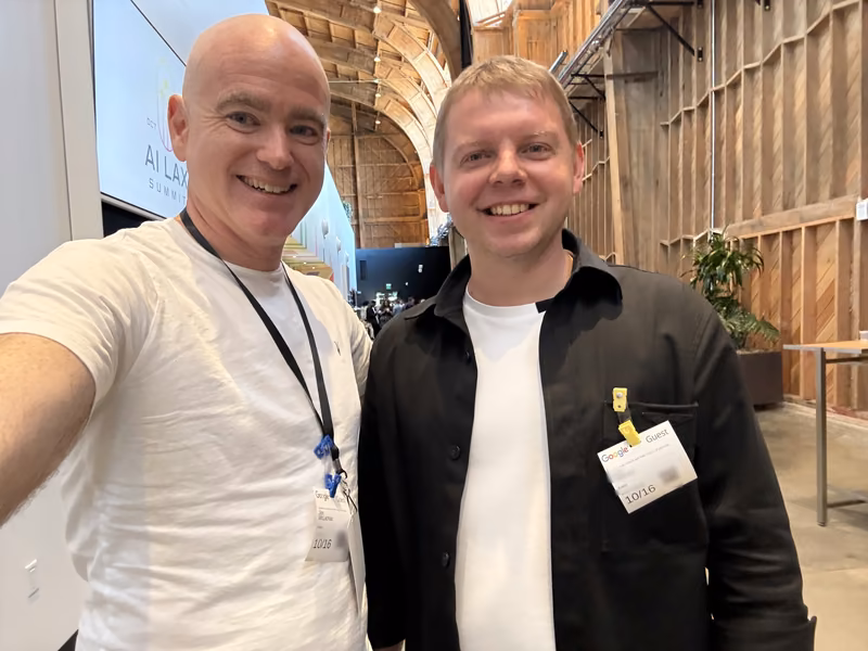 Jon McLachlan of YSecurity taking a selfie with a fellow attendee inside Google’s wooden hangar in Playa Vista, an AI LAX Summit screen behind them