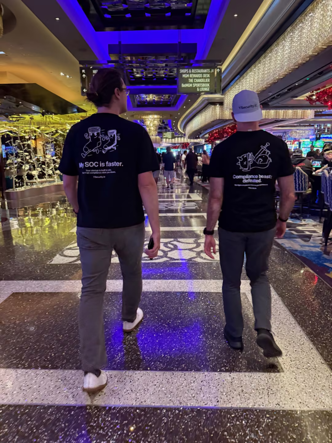 Two YSecurity engineers crossing a Las Vegas casino floor at Black Hat USA 2026 in team shirts reading My SOC is faster and Compliance beast: defeated